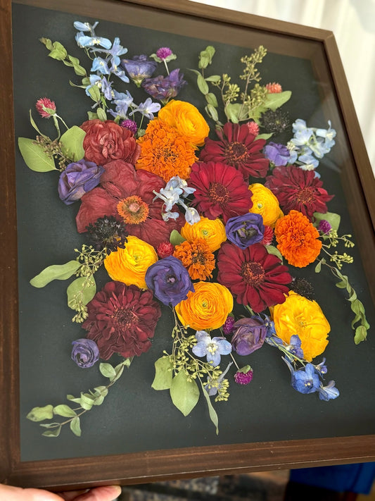 Framed pressed flower arrangement with a variety of colors on a dark background
