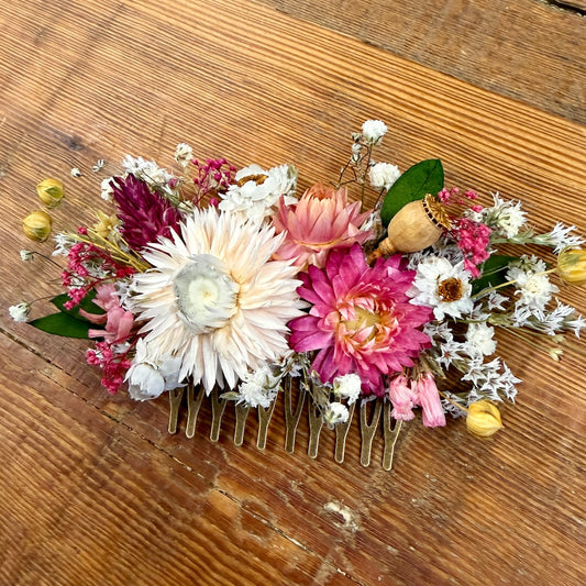 Floral hair comb with pink, white, and green flowers on a wooden surface